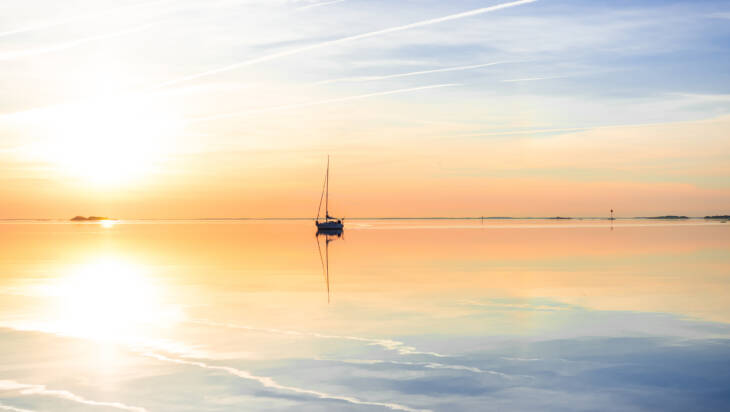Solnedgång på ett lungt hav samt en segelbåt