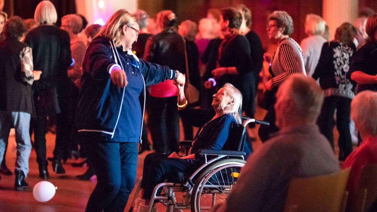 Diskotanssit iäkkäille kaupungintalon juhlasalissa. Rullatuolissa istuvaa naista tanssittaa naishenkilö.